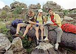 Drei junge Wanderer sitzend auf Baumstamm, Karte überprüfen.