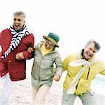 Three mature friends arm in arm on beach, portrait