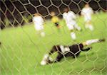 Goal keeper defending goal during a match, blurred, seen from behind net.