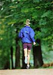 Woman in sports clothes running, rear view, trees in background