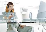 Woman wearing headset, sitting at desk, three quarter length