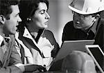 Three people with laptop computer, one with hard hat, head and shoulders, b&w