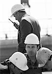 Four men with hard hats, one holding walkie-talkie, b&w