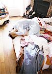 Woman huddled up on bed among clothes with hands on head