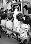 Children on bench, one putting finger up, rear view, b&w