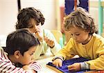 Three children sitting at table, one sewing