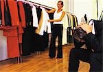 Woman in store looking through clothes, man sitting with head down and hands on neck
