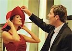 Woman trying on hat for man, man flipping front of hat.