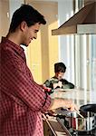 Father cooking, son in background looking at book.