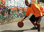 Man dribbling basketball next to graffitied wall, close-up