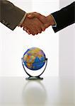 Two businessmen shaking hands above globe