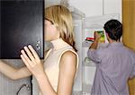 Young couple in kitchen, woman opening cupboard, man taking item from refrigerator