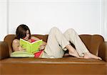 Woman lying on sofa, reading book