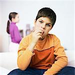 Boy sitting on sofa, eating, girl standing in background