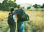 Couple walking with arms around each other through field, rear view