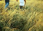 Couple running in field of tall grass, mid-section