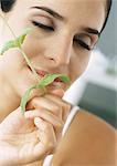 Woman holding sprig of mint under nose, eyes closed, close-up