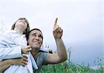 Man holding son in arms pointing to overcast sky