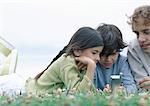 Boy and girl with father lying on stomachs on grass looking at cellphone