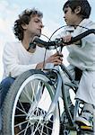 Garçon sur vélo regardant père agrippant à bicyclette, vue d'angle faible