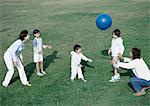 Eltern mit jungen und Mädchen spielen Ball auf Gras, in voller Länge