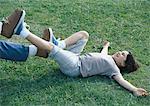 Boy lying on back on grass with feet pushing against man's feet