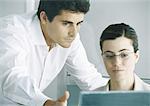 Woman working at computer, male colleague leaning over shoulder, gesturing to screen