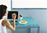 Woman sitting at table with laptop, eating fruit