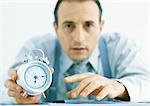 Man holding out alarm clock, focus on hands and clock in foreground