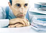 Man resting head on hands, looking at stack of files