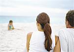 Parents assis sur la plage en regardant la petite fille jouant dans le sable