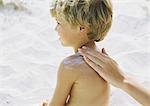 Little boy on beach having sunscreen rubbed into shoulder by mother