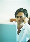 Man with serious expression using cellphone while looking at laptop computer