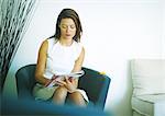 Woman sitting in chair, writing on magazine