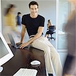 Homme assis sur le bord du bureau au bureau occupé