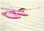 Rosa Flipflops neben Strandmatte am Strand