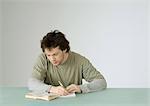 Young man sitting with open book, taking notes