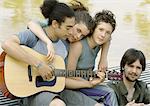 Four young friends gathered around guitar