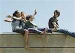 Young people sitting on top of wall with arms out