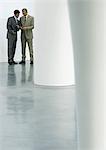 Two businessmen standing in lobby, looking at cell phone