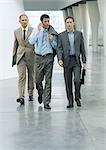 Three businessmen walking through lobby, one using cell phone