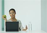 Woman sitting at laptop, holding glass of water and apple