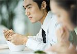 Businessman eating with chopsticks, looking away