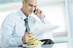 En utilisant le téléphone et journal de lecture, hamburger sur table au premier plan de l'homme