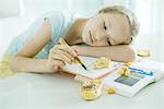 Girl sitting at table doing homework, resting head on arm, doodling, food scattered on books
