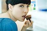 Woman eating piece of chocolate cake, looking over shoulder at camera