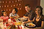 Family with two children eating festive dinner, smiling at camera