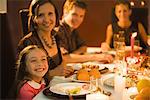 Family eating festive dinner, looking toward camera, smiling