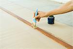 Woman painting wood plank with paintbrush, cropped view of hand