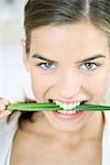 Woman holding chives between teeth, smiling at the camera, portrait